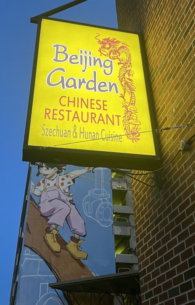 The logo of the Beijing Garden Chinese restaurant is yellow with red highlights and on the building behind it is a large art mural.