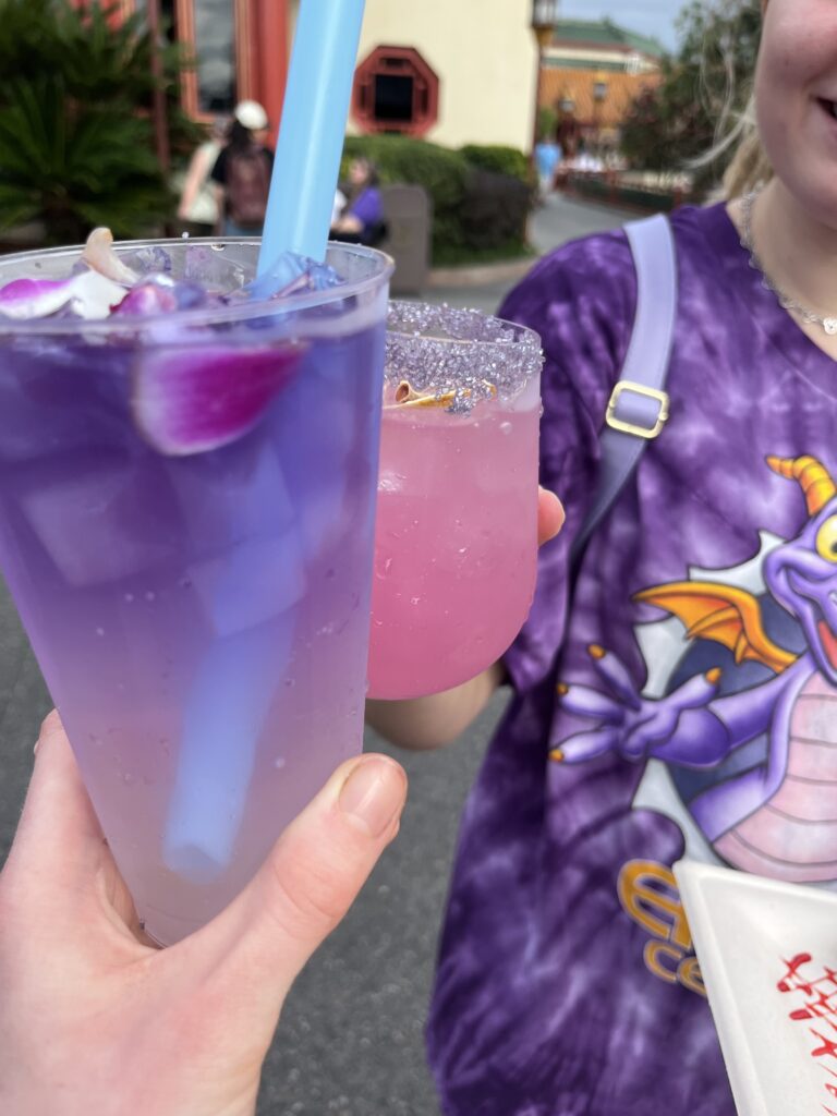 Maddie and Bri toast together a blue and a pink drink.
