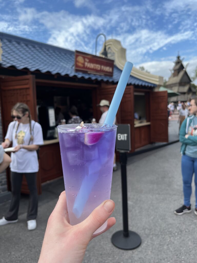 A lavender colored drink with a purple flower, boba pearls, and boba straw.