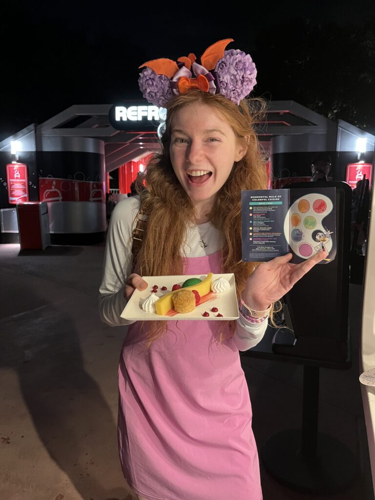 Bri smiles holding up the stamped page of the festival of the arts guide and a deconstructed key lime pie in her other hand.