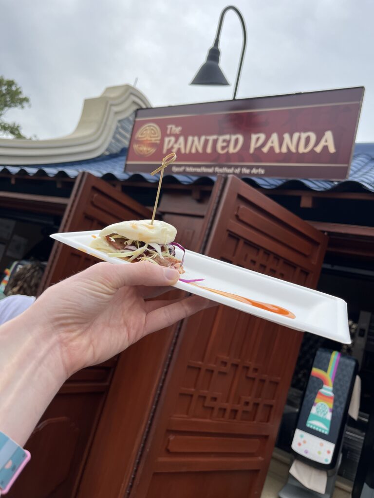 A bao bun held up in front of the Painted Panda Food booth.
