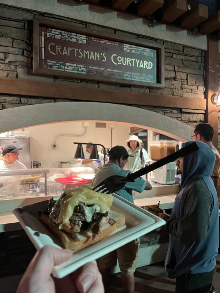 Grilled pork belly sandwich held out in front of the Craftman's Courtyard food booth.
