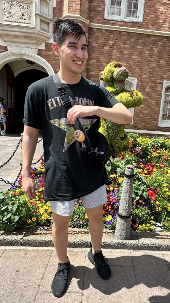 Alix poses with his arm bent out in front of him smiling with a topiary of Tigger posed the same way behind him.
