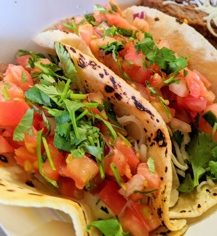 Tacos covered with tiny diced tomatoes and cilantro in a flour tortilla.