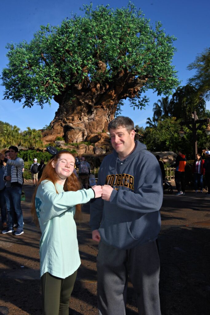 Bri and her dad give eachother a fistbump smiling proudly in front of Animal Kingdom's tree of life.