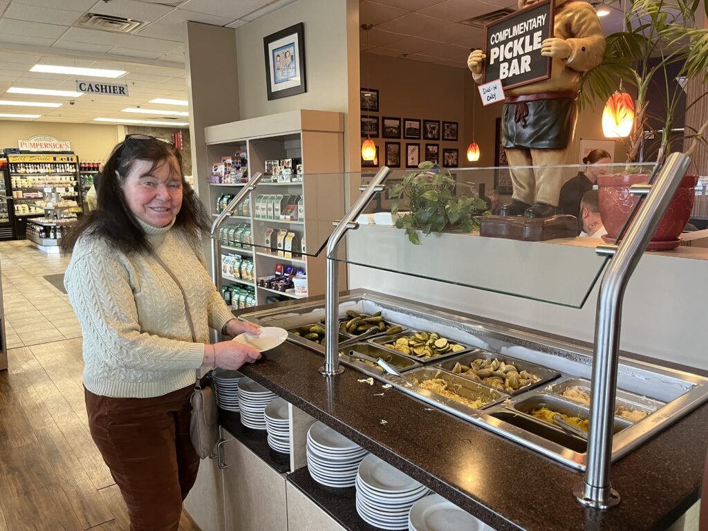 Nana stands smiling by a self-service 'pickle-bar'