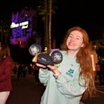 Bri holds her graduation ears and smiles in front of Tower of Terror