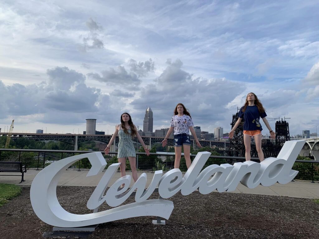 The Cleveland sign with Bri and her sisters posing on the letters. The city of Cleveland can be seen behind.