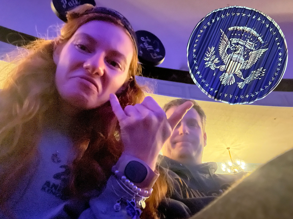 Bri and Dad make a funny face looking down at the selfie camera. The picture has photoshopped in the Hall of Presidents logo of an american eagle circled by stars and olive branches.