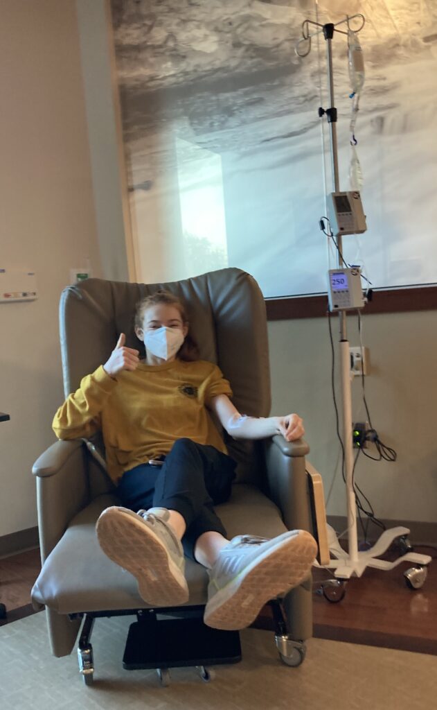 Picture of Bri in Hospital receiving a transfusion. She holds a thumbs up.