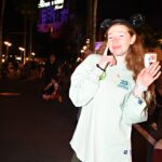 Bri makes a sad face and hand gesture of a 'tear' down her face as she waves goodbye to the camera in front of Tower of Terror.