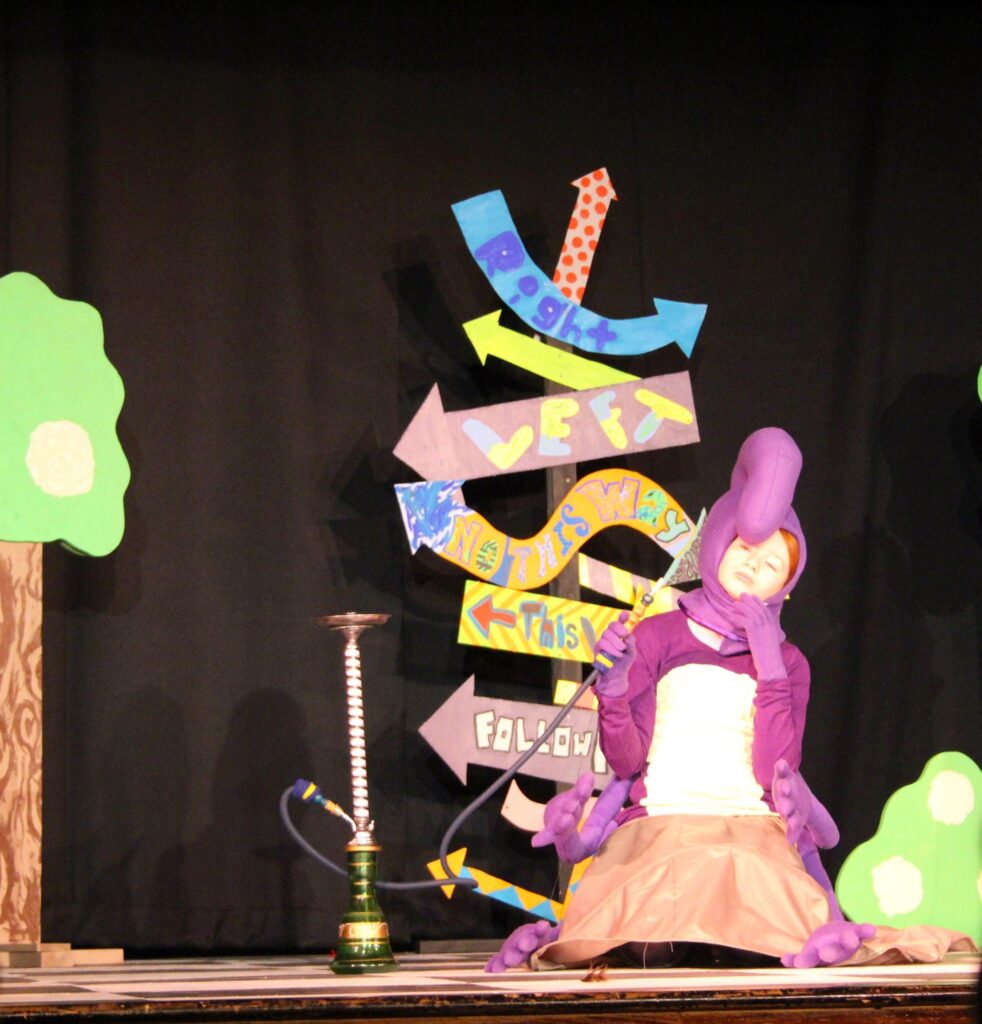 Bri dressed up like a caterpillar rubbing her chin in thought as she plays the caterpillar in Alice in Wonderland