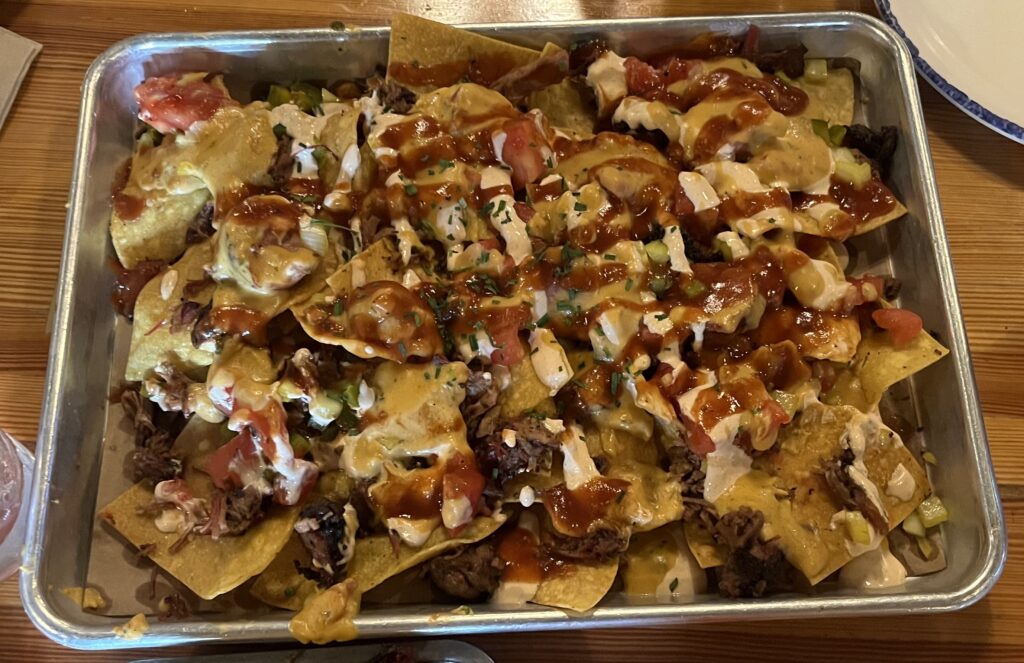 A plate of nachos with crema, jalepenos, fried tomatoes, cheese, and brisket.