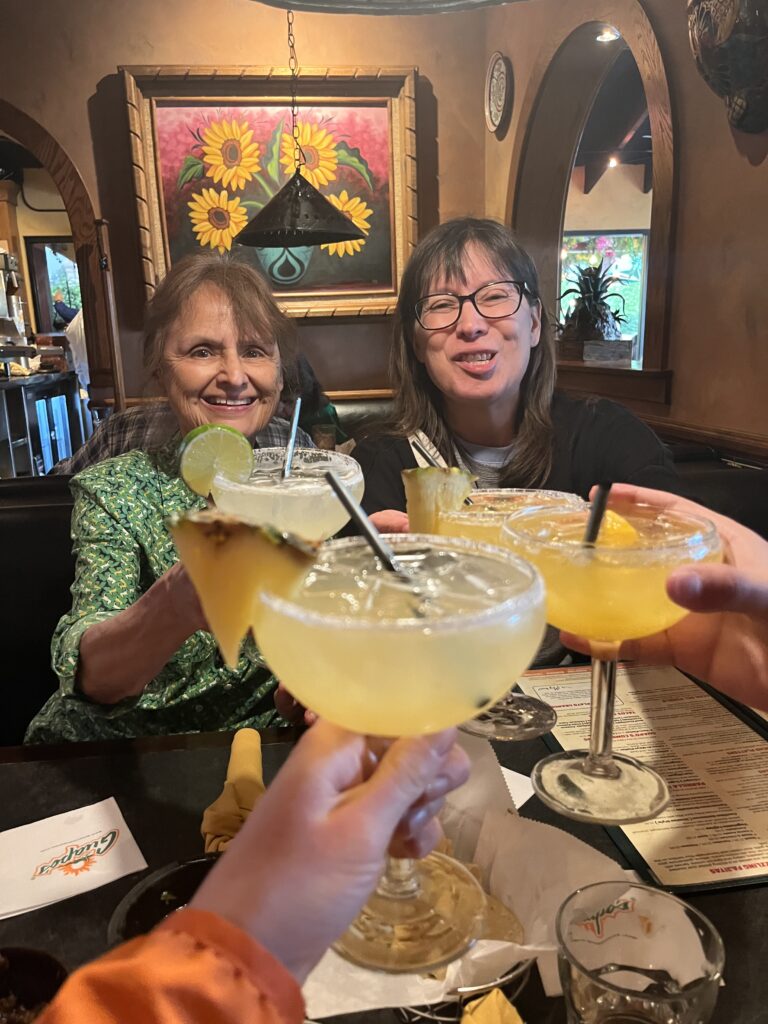Gerri and Lulu in the background giving cheers with Alix and Bri who's arms and margaritas are only shown.