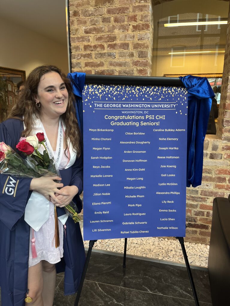 Megan stands next to a sign that lists all the graduates from a Psychology honors society.