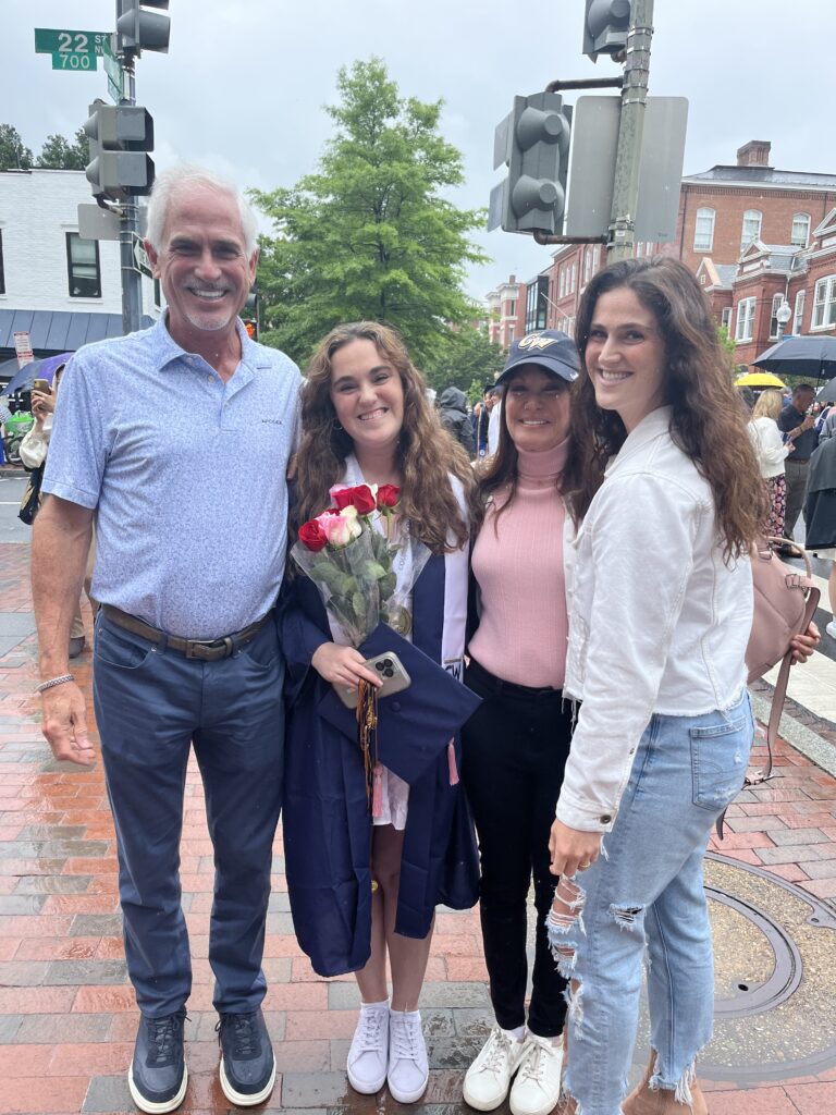 Megan in cape and gown holds flowers and smiles in a photo with her family.