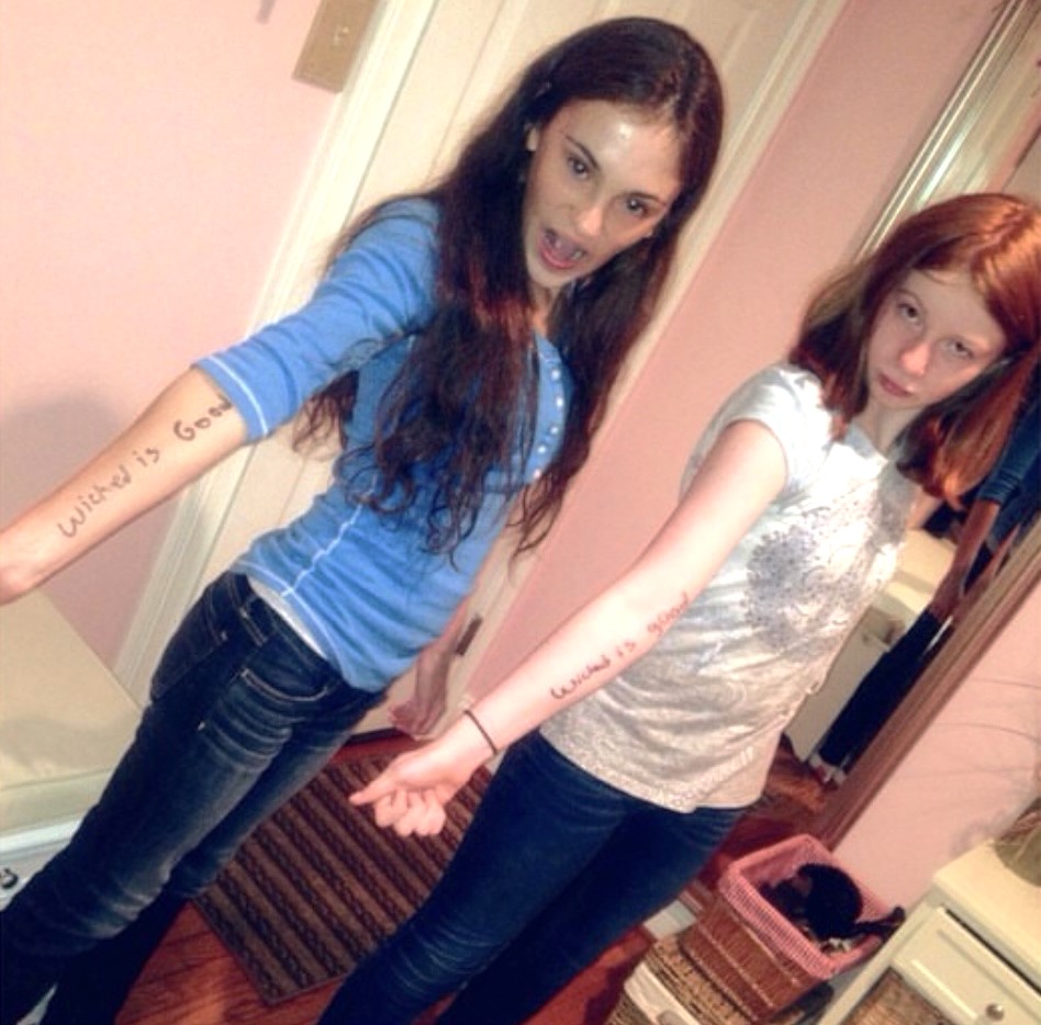 Megan and Bri hold out their arms which has sharpied "Wicked is good on them".