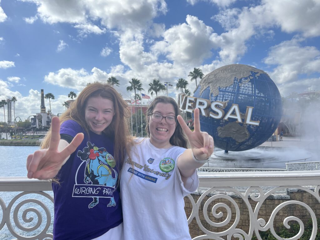 Bri and Sarah hold up two fingers in front of the Universal Studios globe logo.