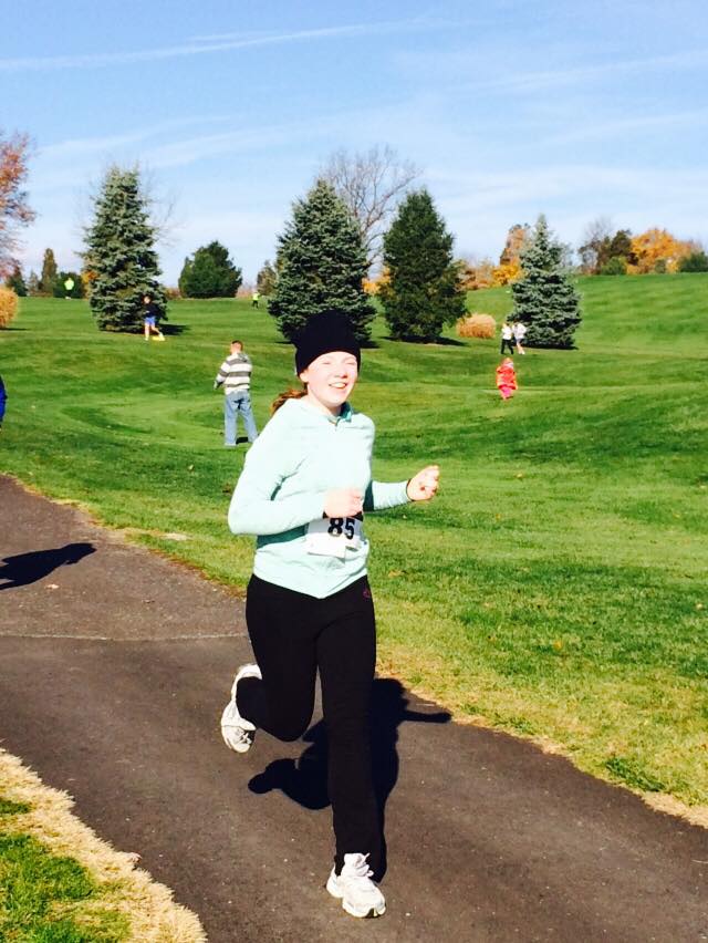 bri wears a black beanie, blue jacket, and black yoga pants as she runs down a pavement.